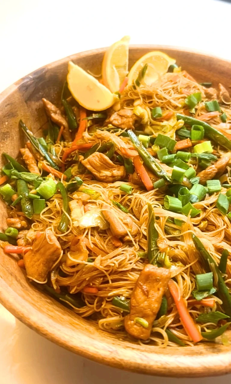Filipino Pancit Bihon featuring thin rice noodles stir-fried with vegetables, chicken, and savoury aromatics, styled in a serving dish