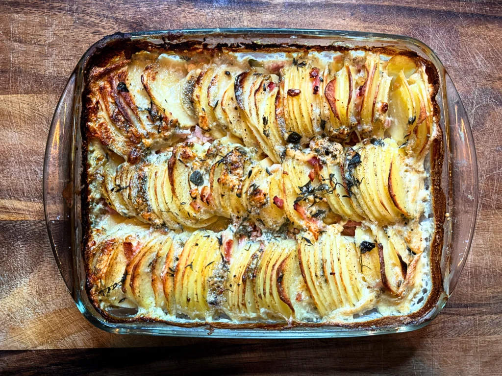 Golden potato dauphinoise-style bake with thinly layered potatoes, crispy bacon, fresh herbs and melted blue cheese, bubbling and crisp on top.