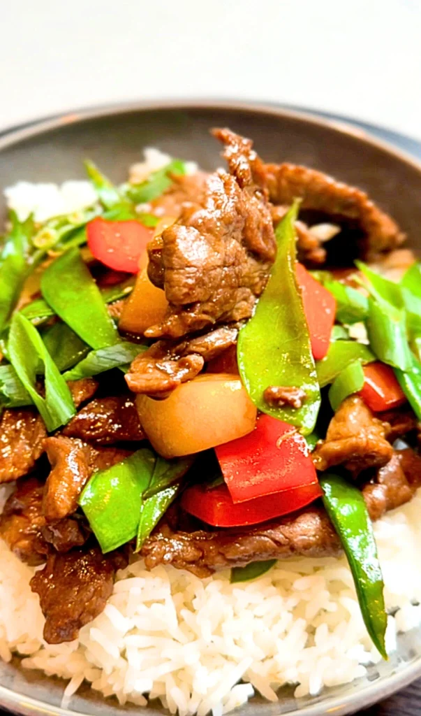 A vibrant beef stir fry featuring silky, thinly sliced beef coated in a glossy savory sauce. The dish is tossed with crisp, colorful vegetables like broccoli and red bell peppers, served in a dark wok to highlight the tender, 'velveted' texture of the meat.