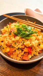 Filipino-style fried rice with crispy spam, pineapple, peas, and green onions in a bowl with chopsticks.